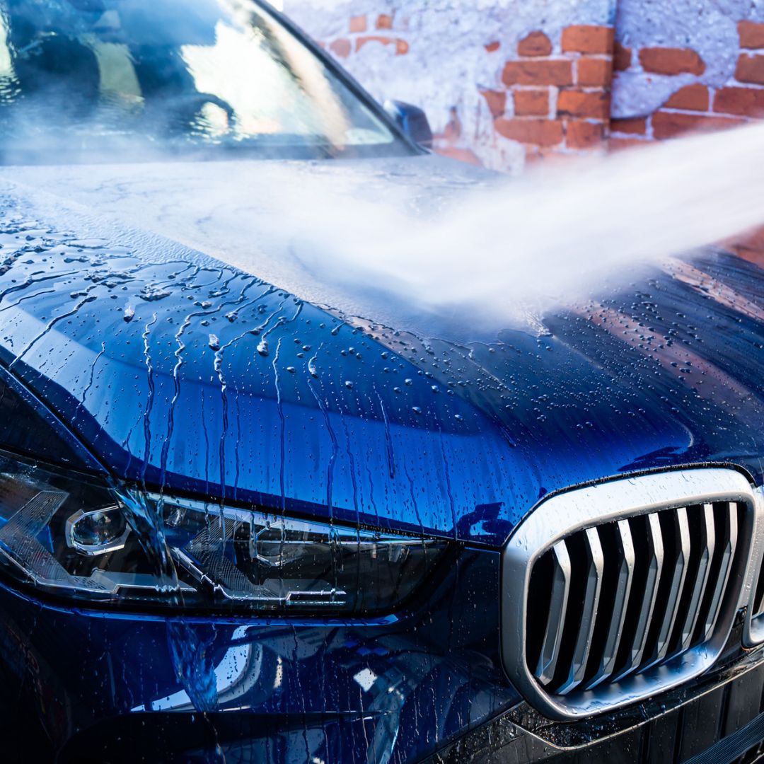 Blue BMW being washed with soap suds on a brick wall background