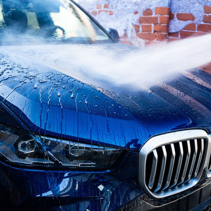 Blue BMW being washed with soap suds on a brick wall background
