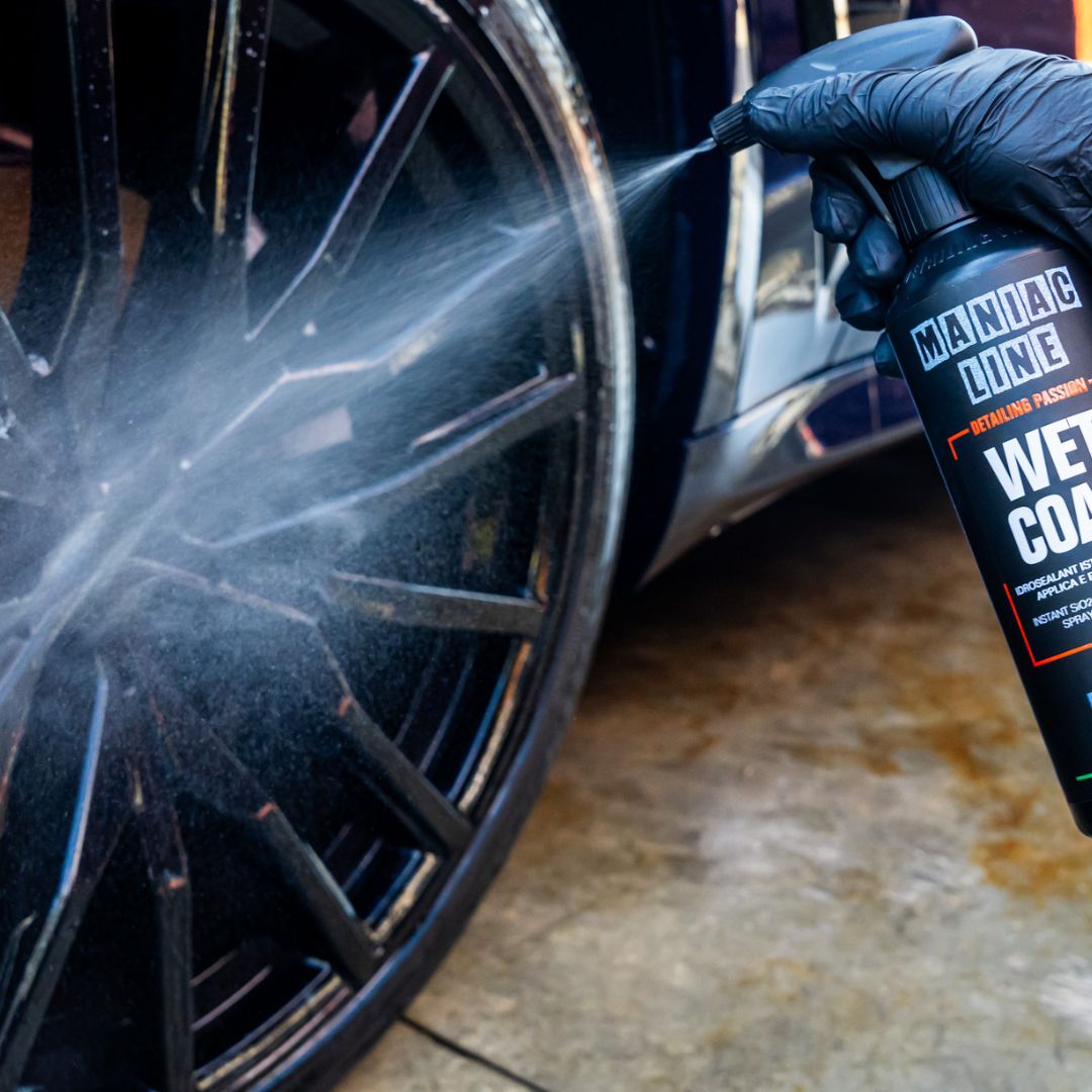 Person applying a Maniac Wet Coat to a car wheel using a spray bottle labeled 'Manic Line'.