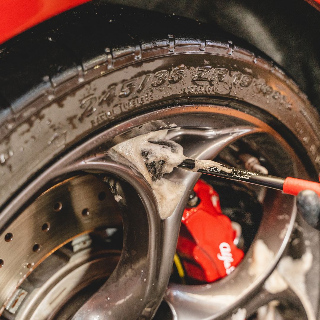 Close-up of a car tire with a wheel brush and brake pads visible