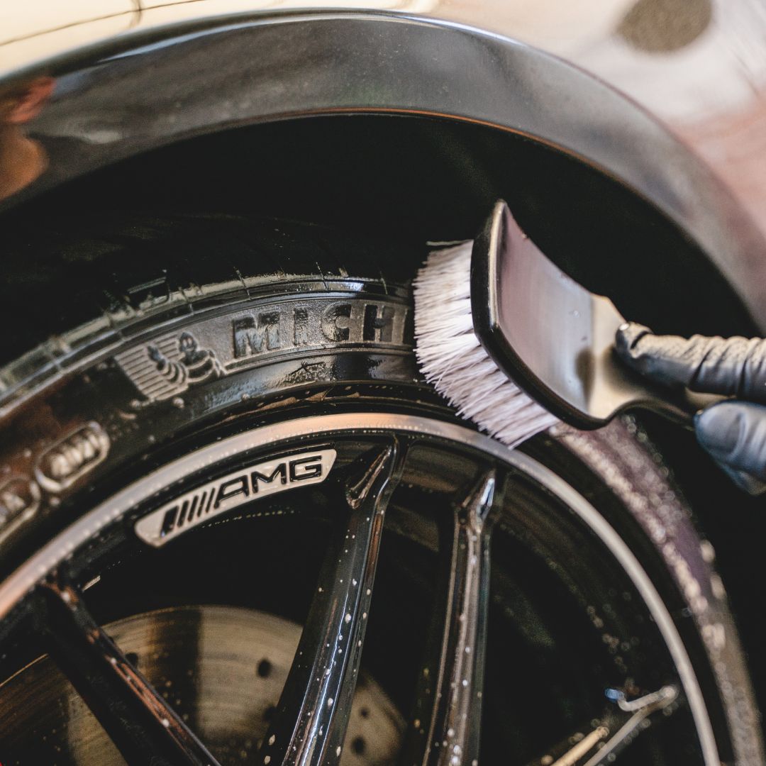 Close-up of a car wheel with a brush cleaning the tire, featuring the AMG logo.