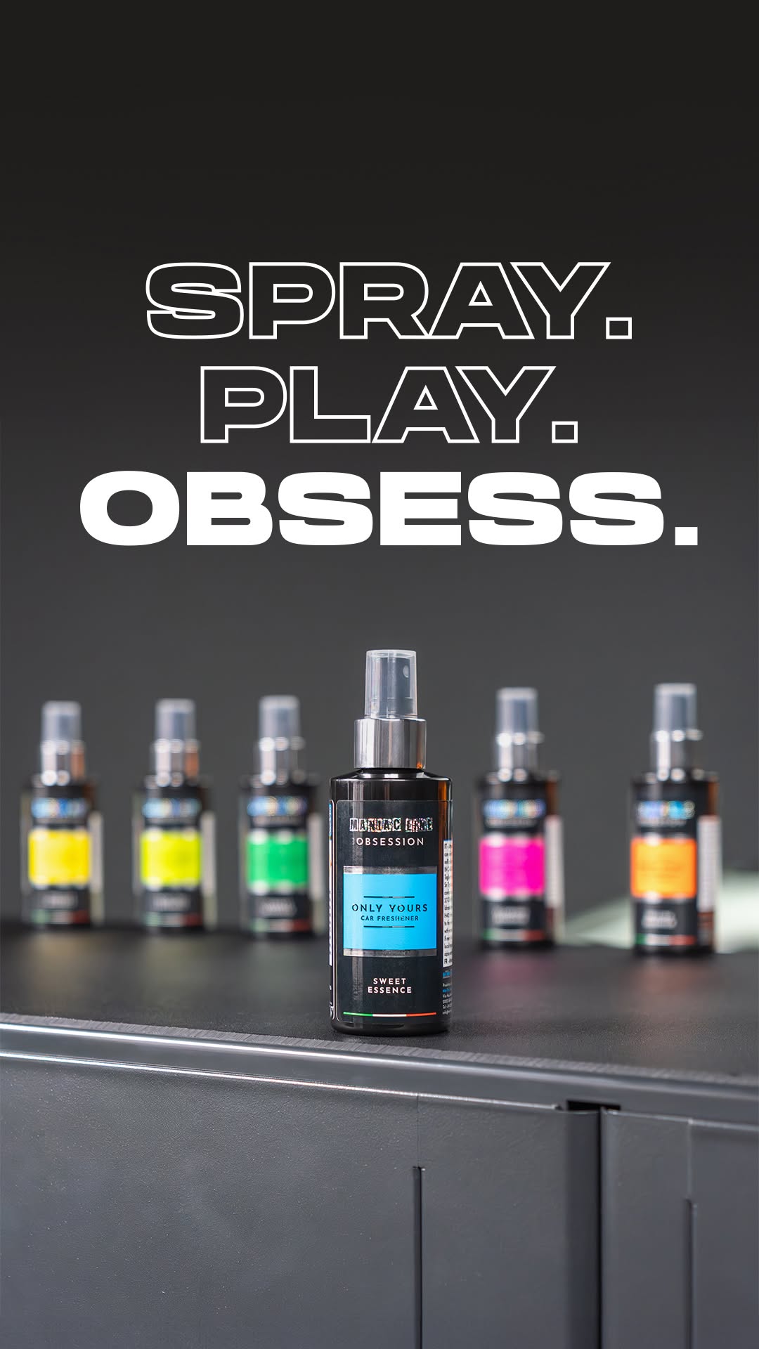 Collection of car air fresheners with colorful labels on a dark surface, featuring the text 'Spray. Play. Obsess.' by maniac line