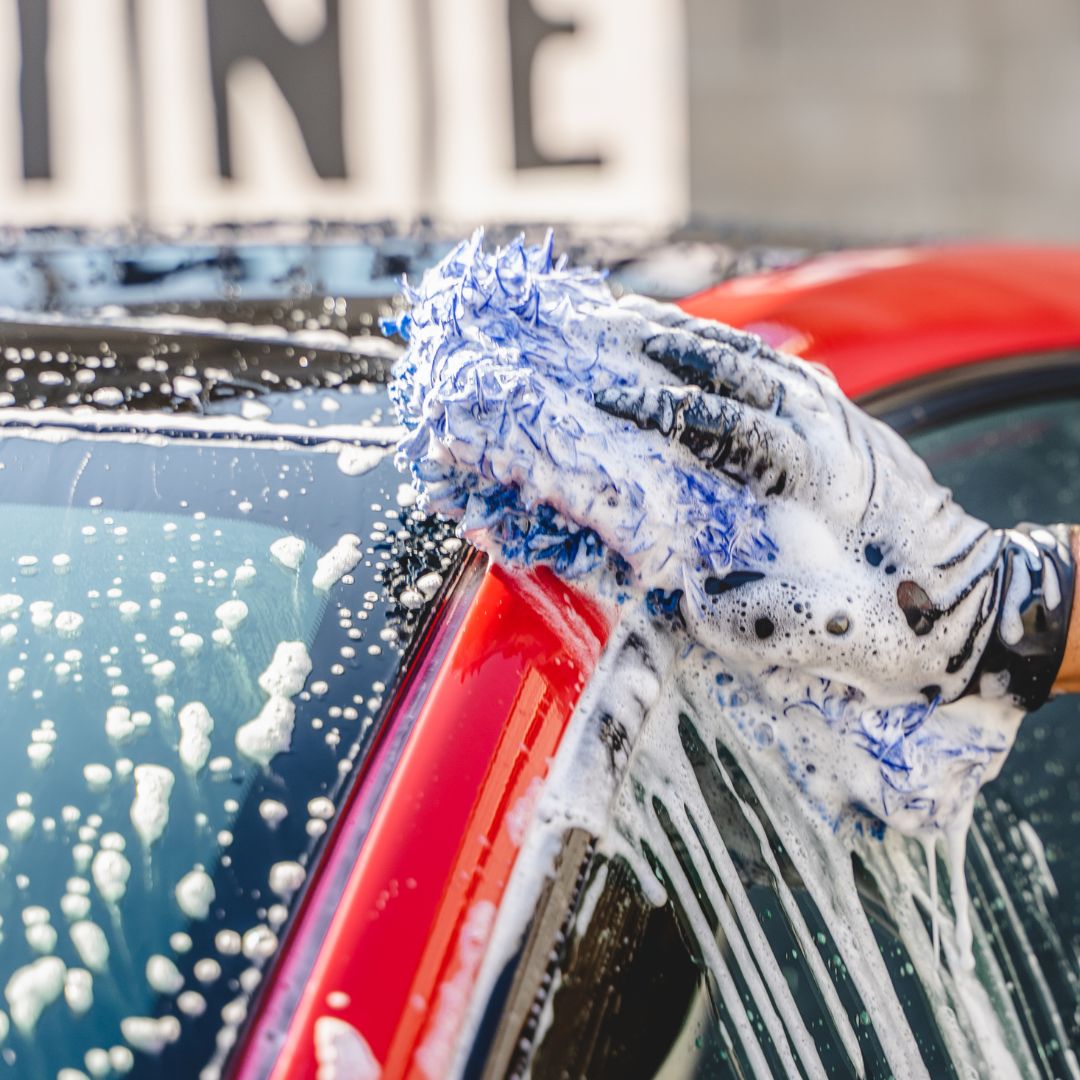 Person cleaning a car with a soapy sponge and glove