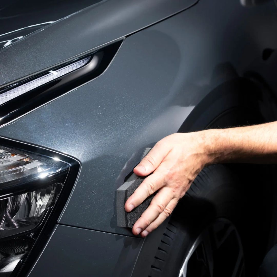 Person holding an Autoglym  precision foam applicator against a grey car.