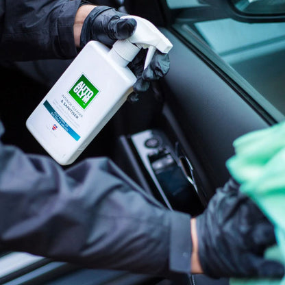 Person cleaning a car interior with a spray bottle labeled Autoglym Interior Cleaner & Sanitiser