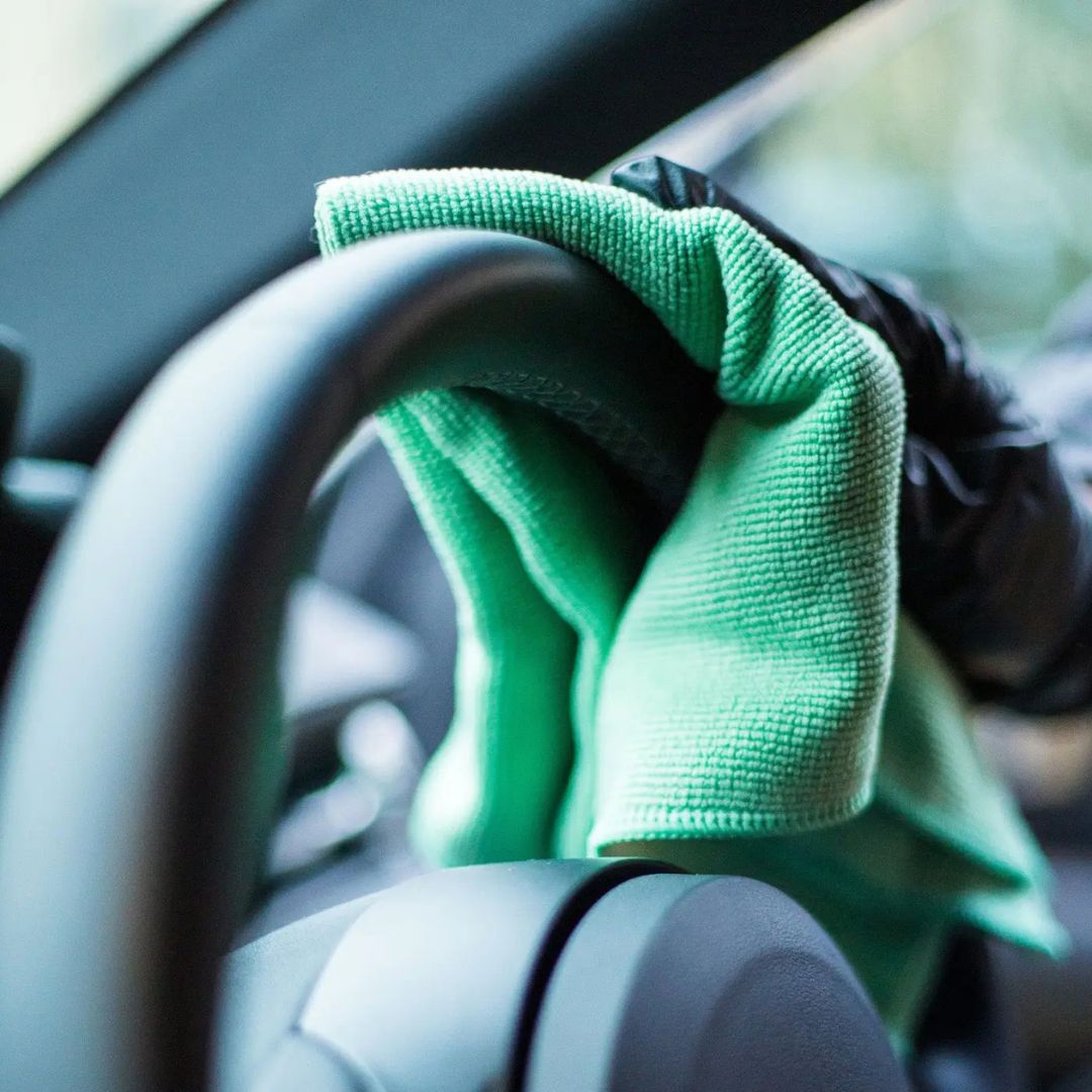 Person cleaning a car steering wheel with a green microfibre cloth.