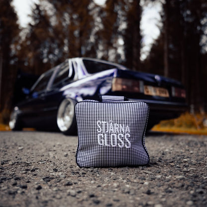 Black and white checkered pouch with 'Starna Gloss' text on a road with a blurred car in the background.