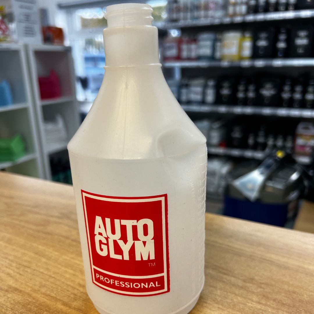 A frosted white plastic bottle of AutoGlym Professional automotive solution, standing on a wooden counter with a blurred store background.