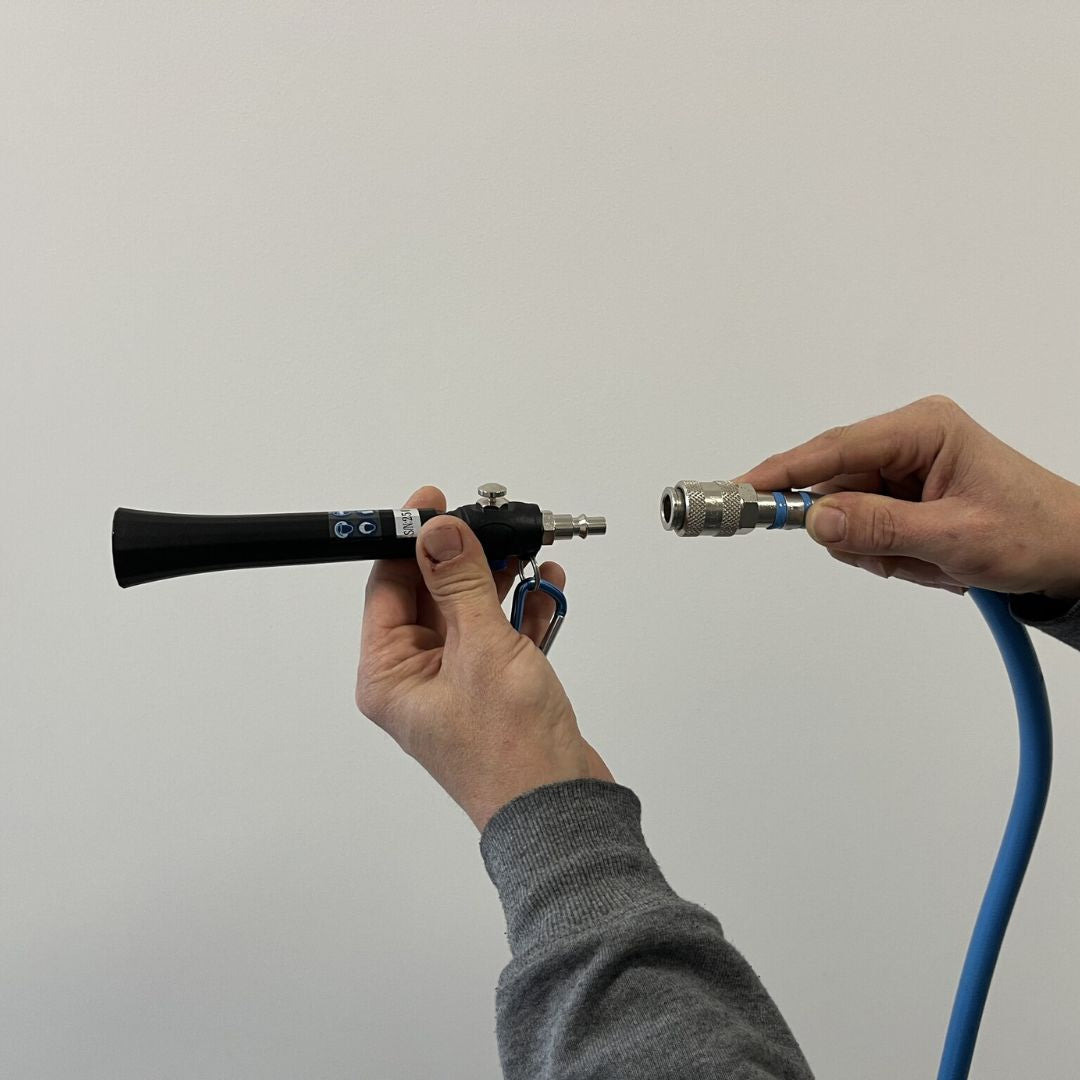 Two hands holding a mini air gun device with a blue hose against a plain background