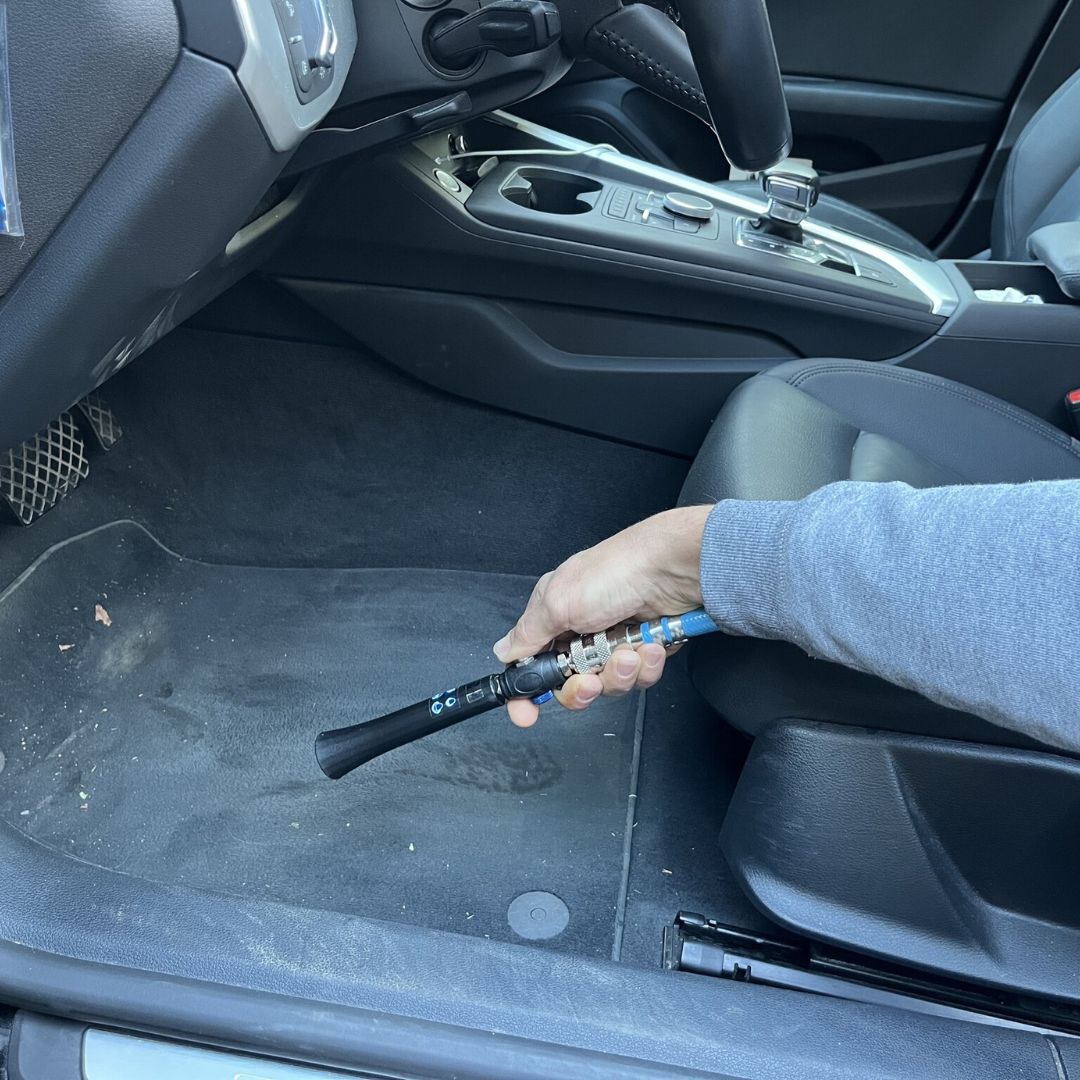 Person holding an air tool inside a car, likely performing maintenance or repair work.