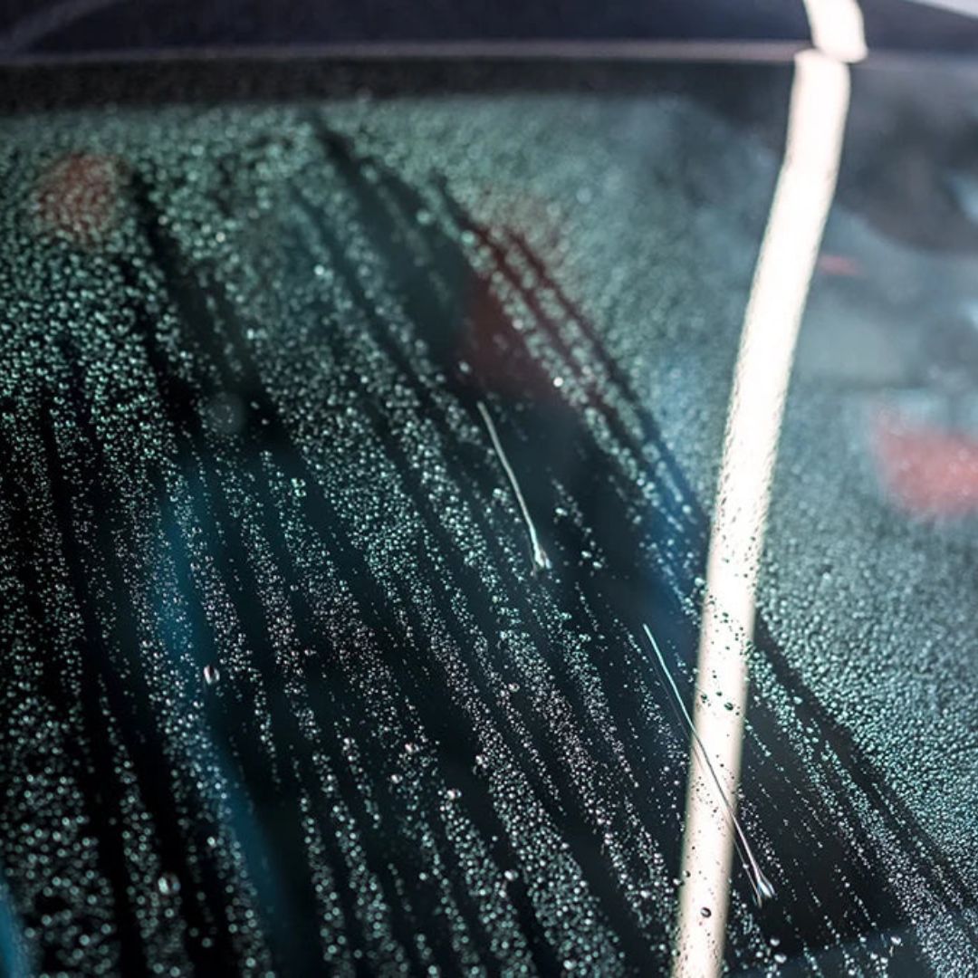 Close-up of a car windshield with water droplets and a wiper blade.