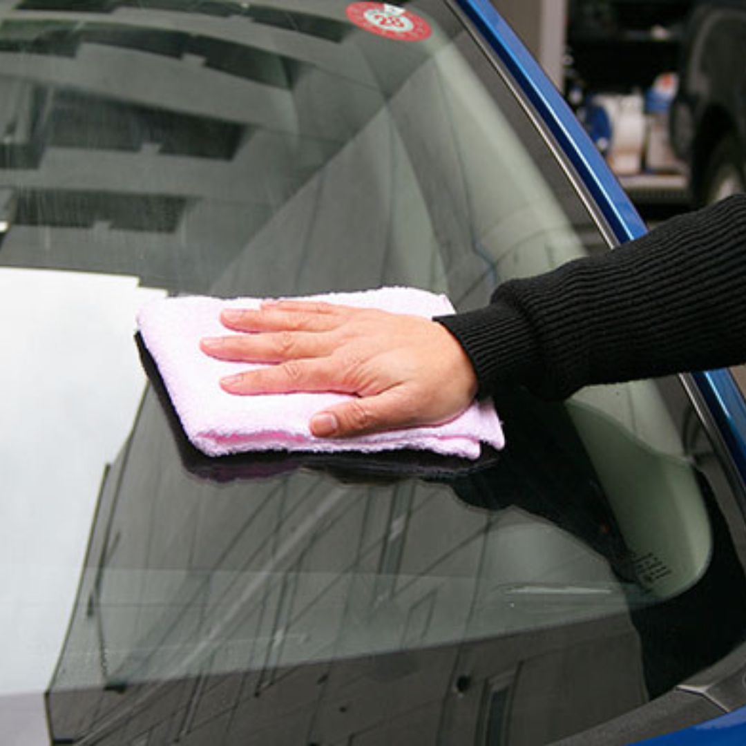Person cleaning a car window with a microfiber cloth