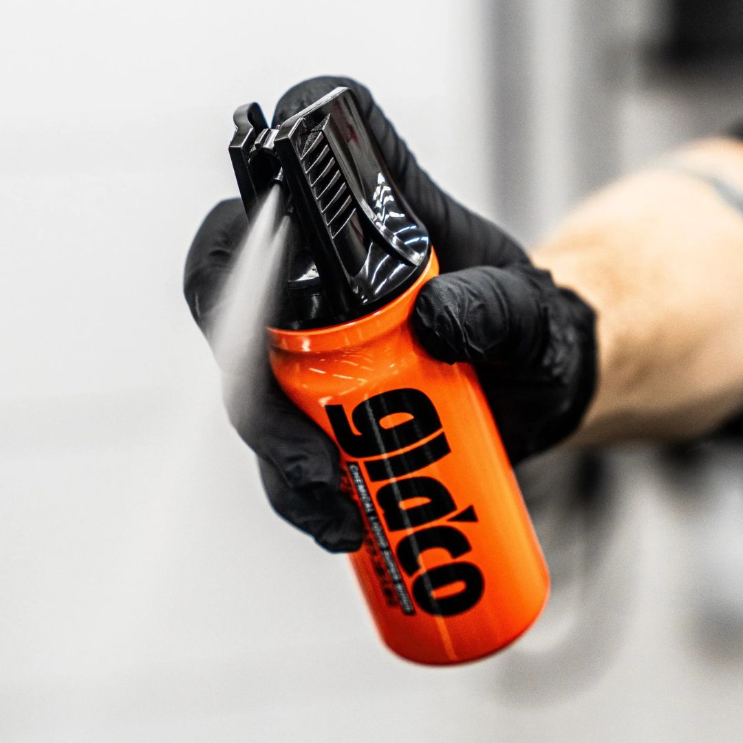 Orange spray can with black nozzle and 'Glaco' branding held by a gloved hand against a neutral background.