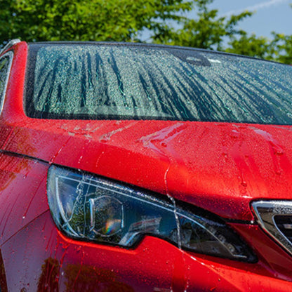 Close-up of a red car's front with water droplets on the windshield and headlight.
