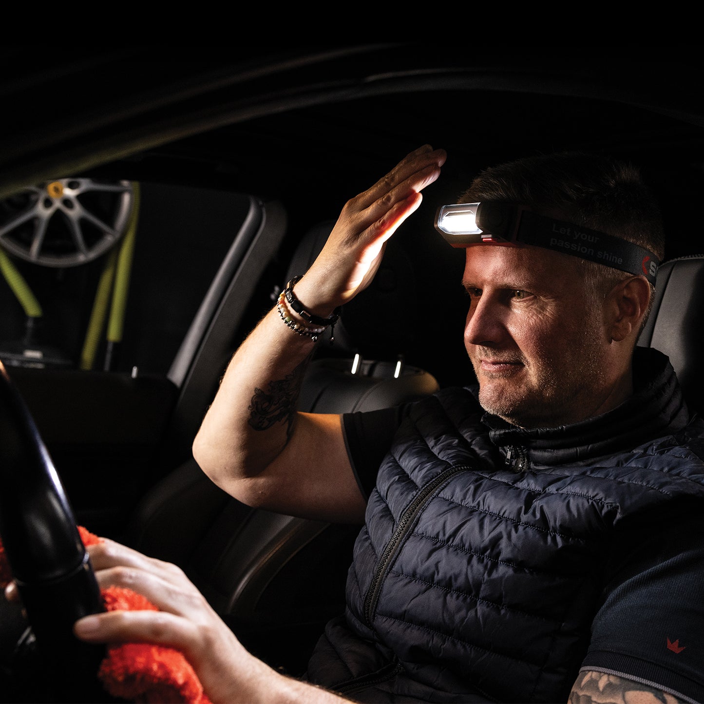 Scangrip I-Match 4  Man sitting inside a car with a headlamp on, adjusting it.