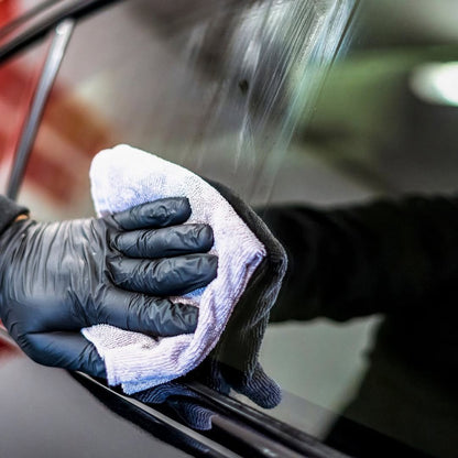Person cleaning car window with a white cloth and black gloves