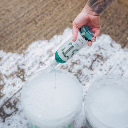 Person pouring stjarnagloss Bubblor from a bottle into a bucket with foam and suds on the ground