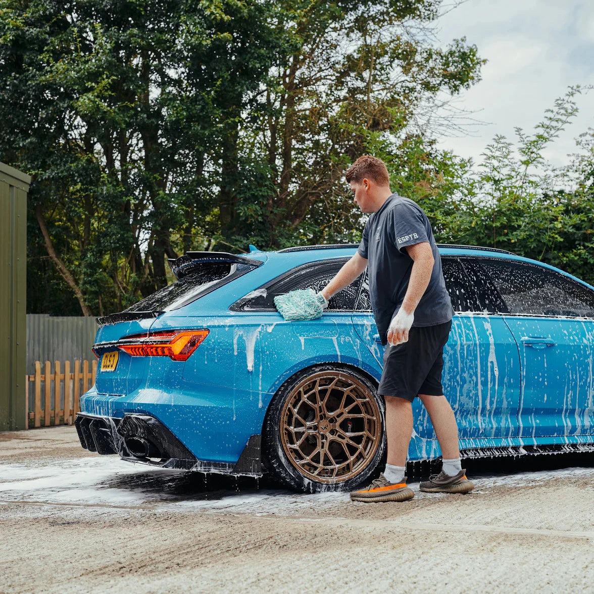 Person washing a blue Audi RS6 with soap suds on a driveway