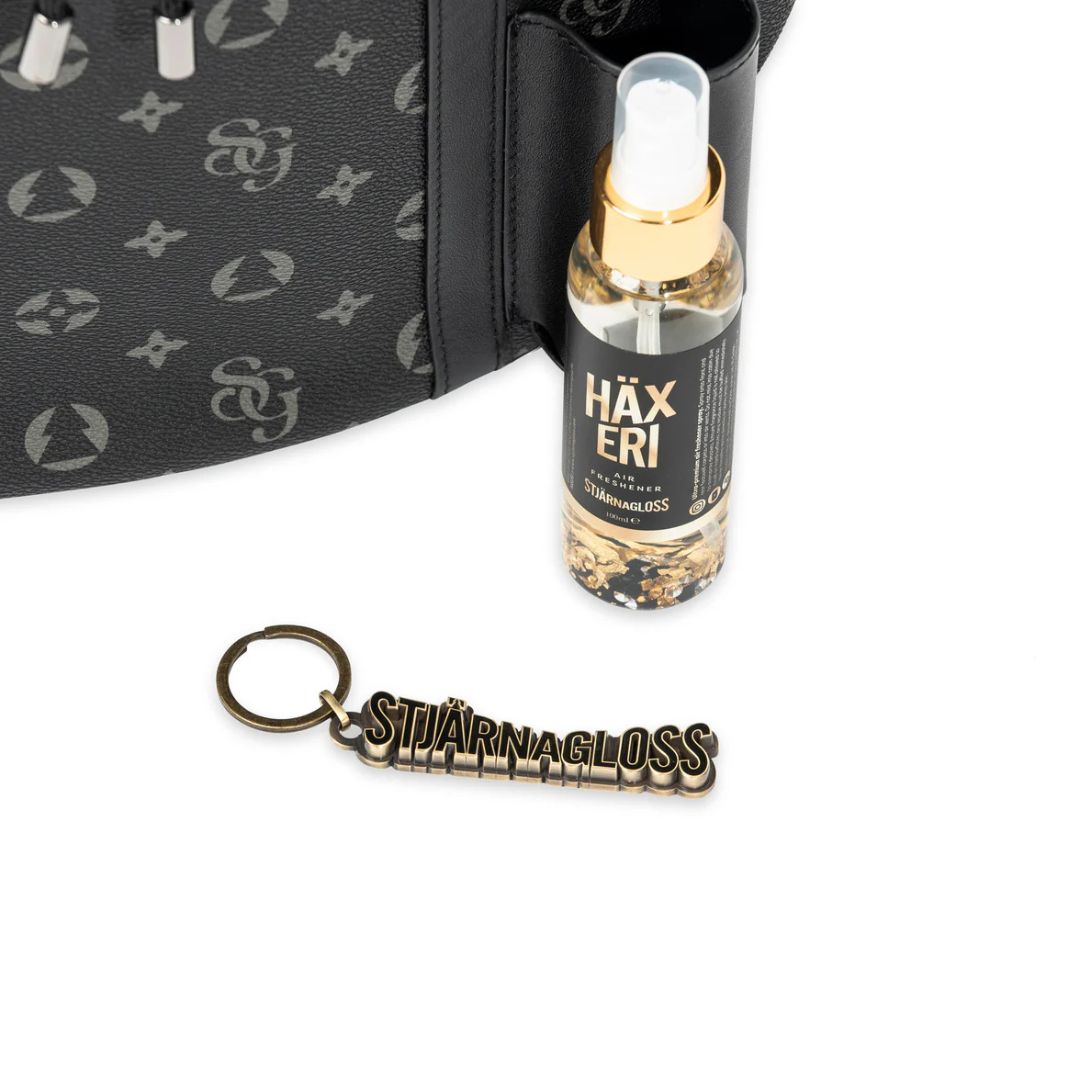 Bottle of Häxeri with a keychain in front of a black bag with a logo.