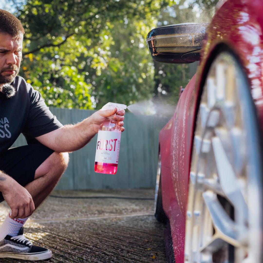 Man cleaning a car door with a spray bottle labeled 'Forst' outdoors.