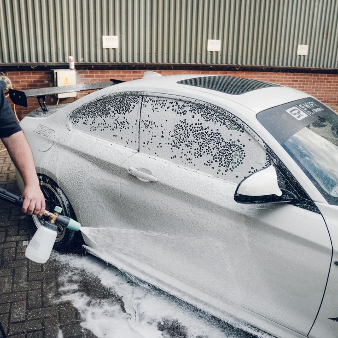 Person washing a white car with soap suds using a high-pressure washer.