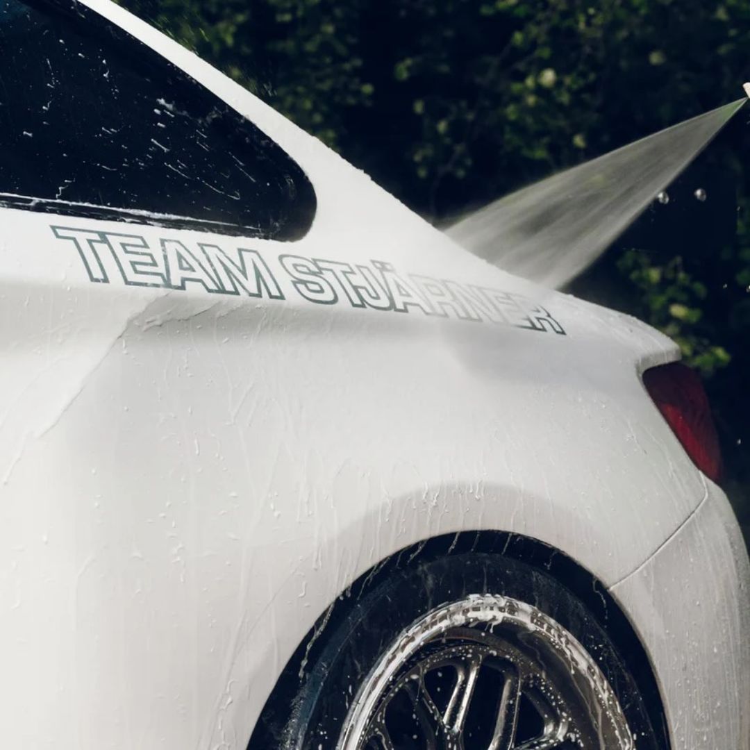White car being washed with a hose, featuring 'Team Stjarnagloss' decal.