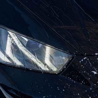 Close-up of a car headlight with water droplets on a dark background