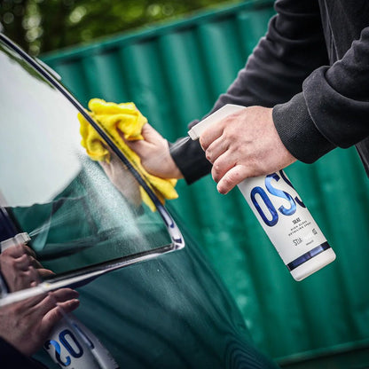 Person cleaning a car window with a yellow cloth and a bottle labeled 'Stjarnagloss Silke'.