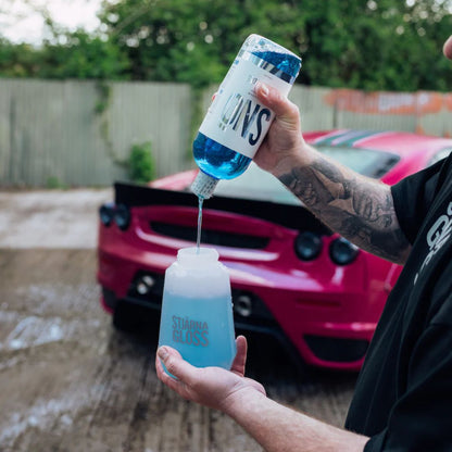 Person pouring Stjarnagloss Sno - pH-Neutral Snow Foam into snow foam gun in front of pink Ferrari