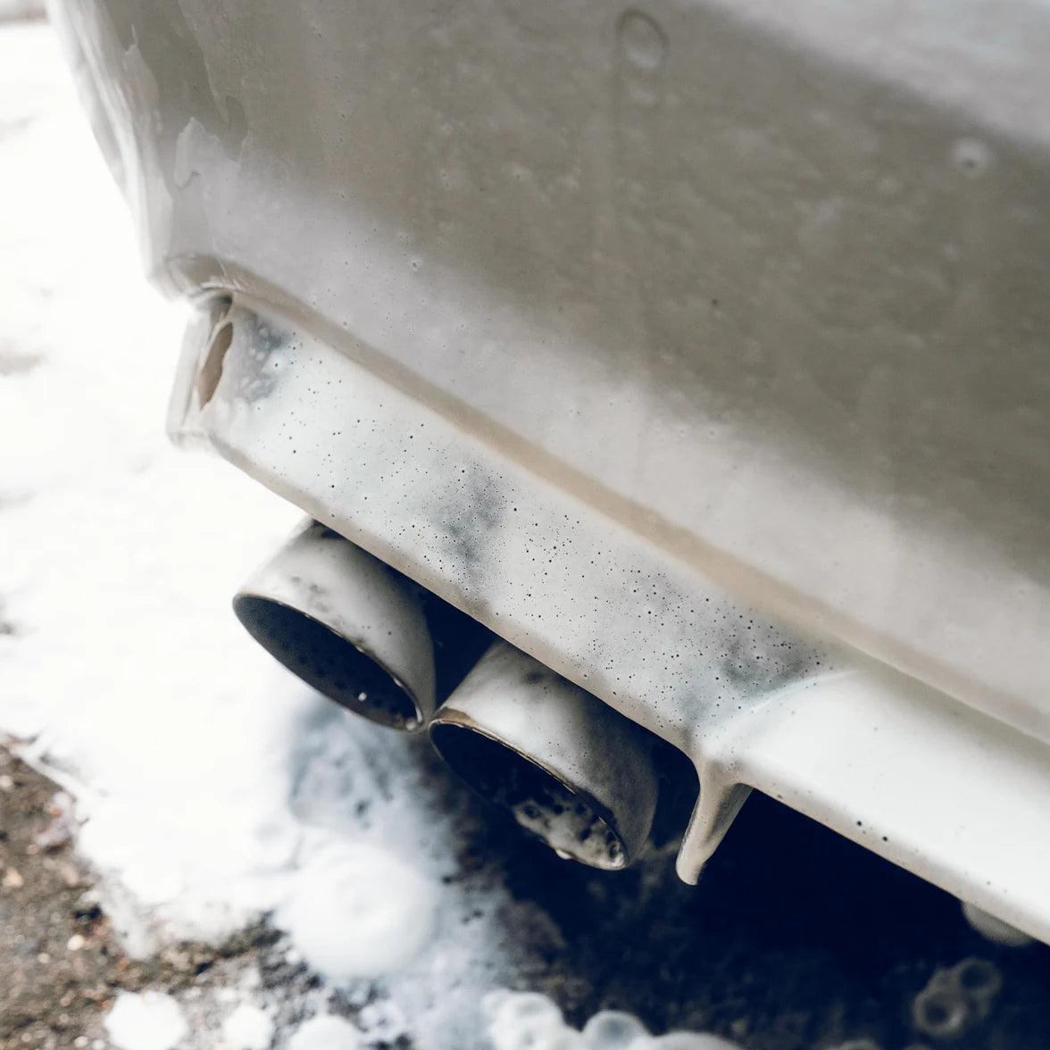 Close-up of a car's exhaust system with snow foam on the ground