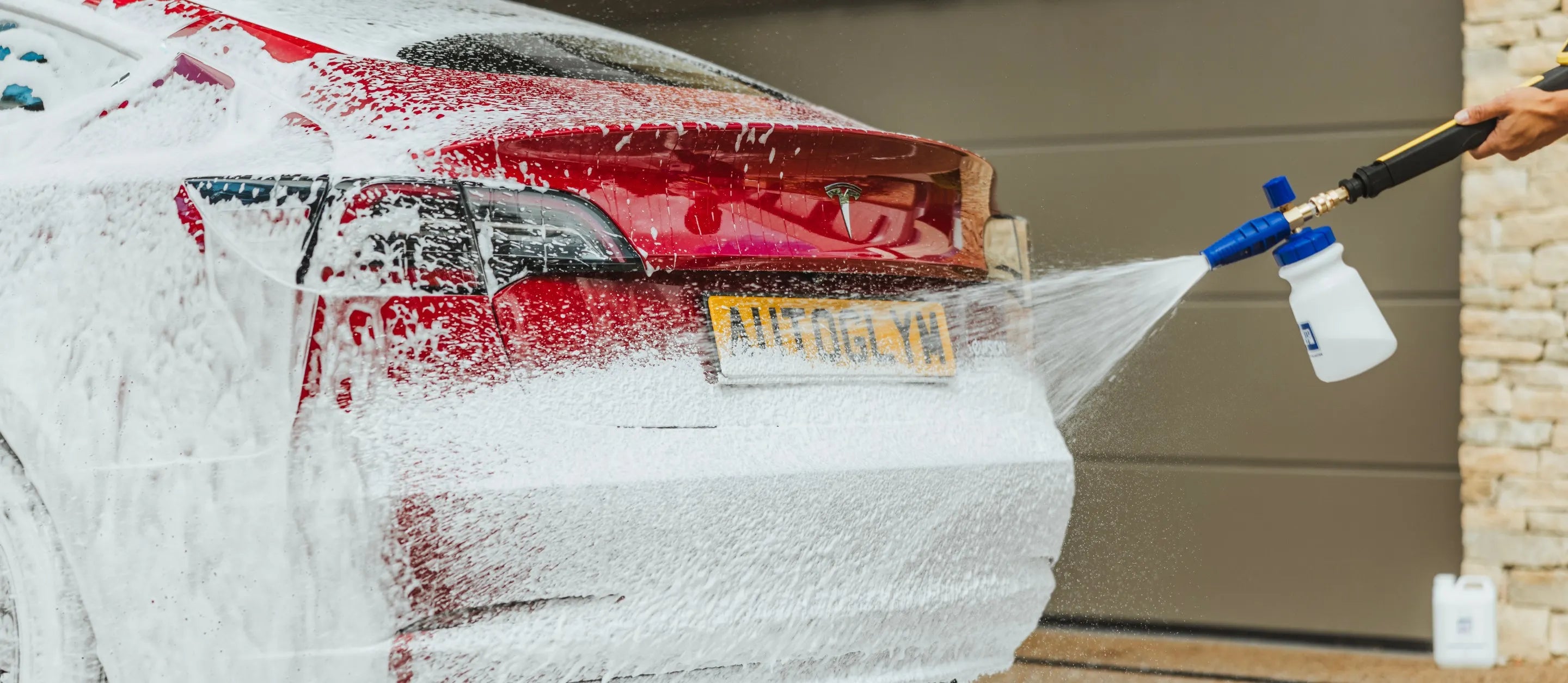 Car being washed with a spray gun in front of a garage door. Autoglym ireland