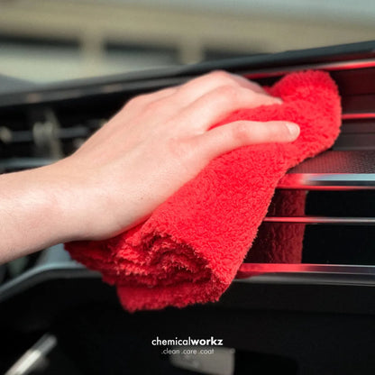 A close-up of a hand wiping a car dashboard vent with a bright red microfiber cloth. The brand name 'chemicalworkz' is visible at the bottom of the image.