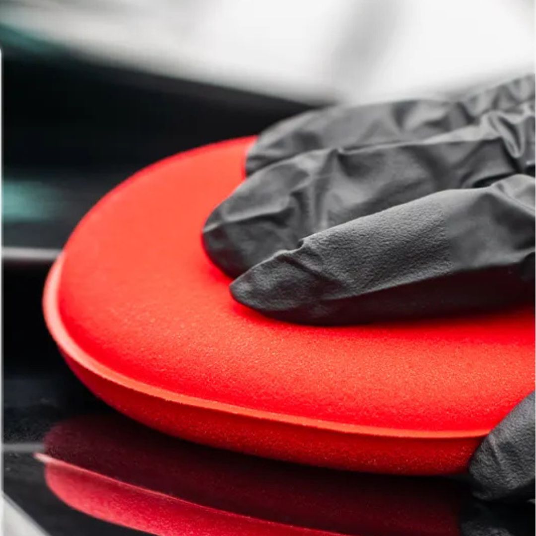 Red applicator with a black glove on a reflective surface