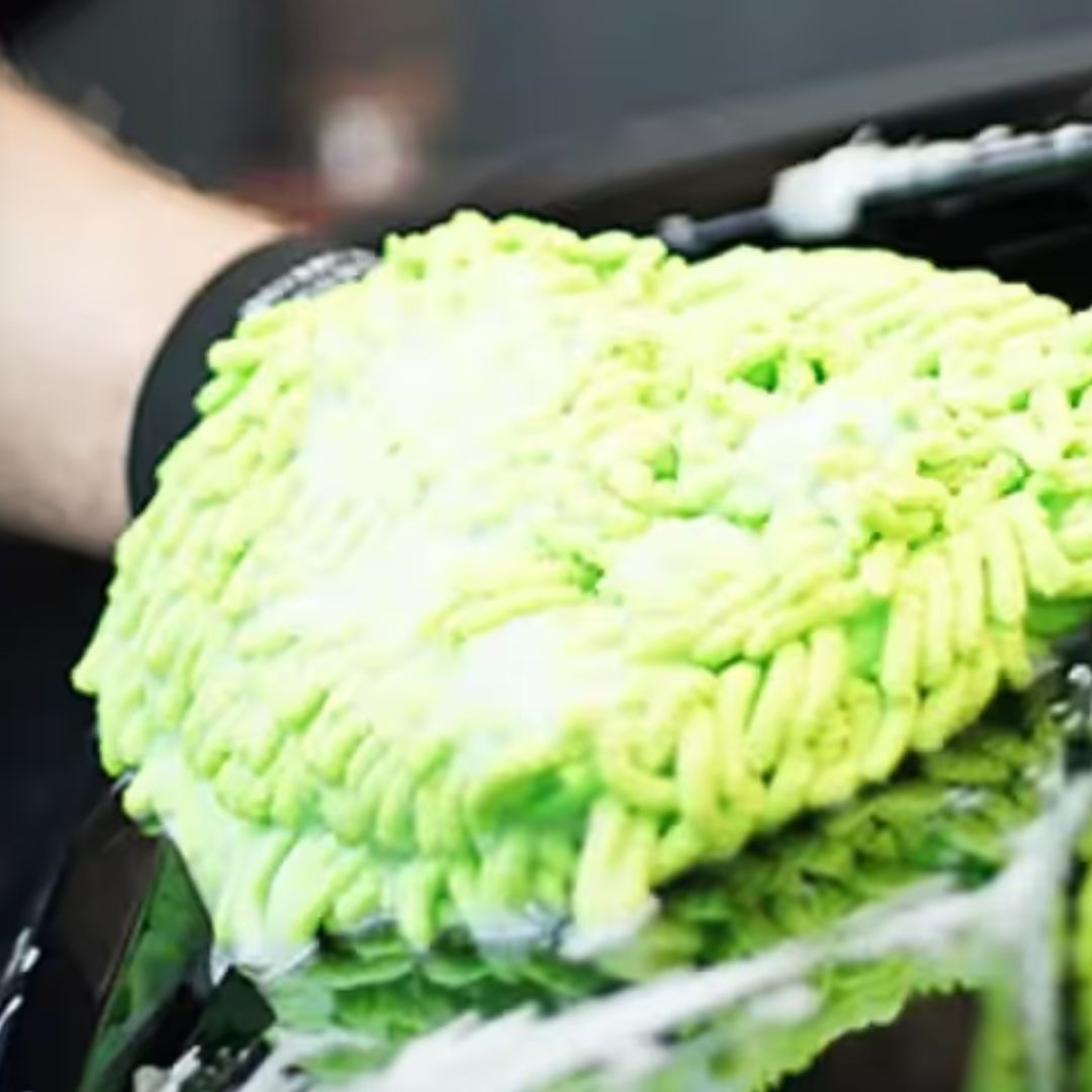 Green chemicalworkz microfiber cleaning cloth on a car window with soap suds.