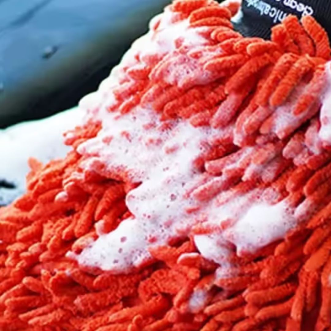 Red cleaning mitt with soap suds on a car surface