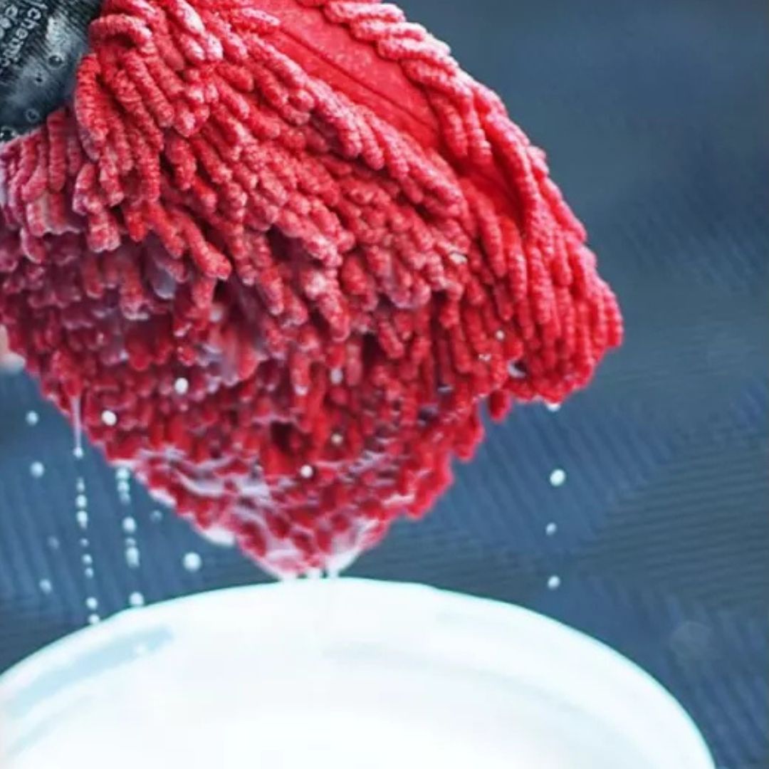 Red microfiber chemicalworkz wash mitt being wrung out over a white container with water droplets.