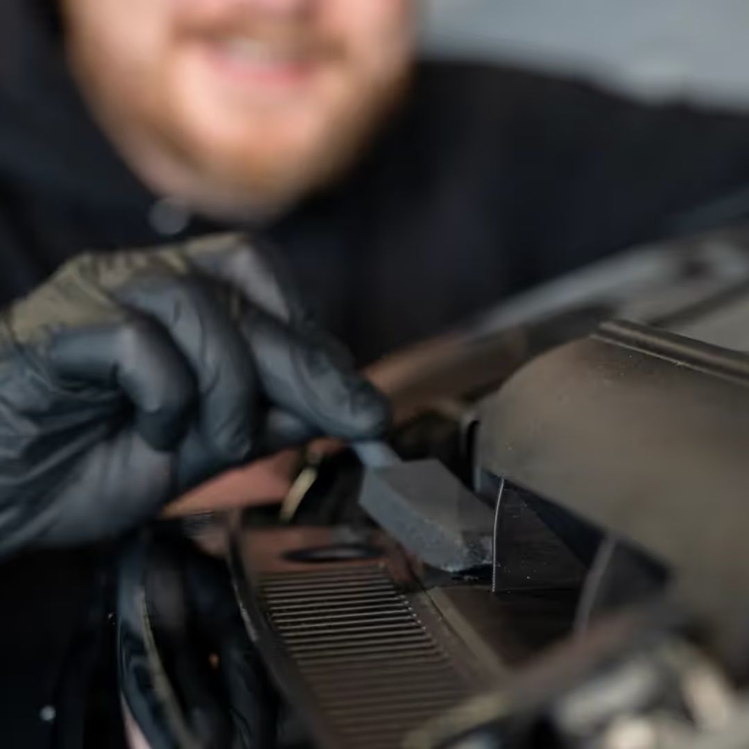 Person wearing black gloves working on a car engine with a blurred background