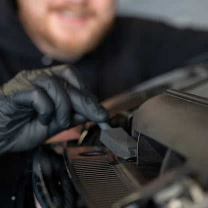 Person wearing black gloves working on a car engine with a blurred background
