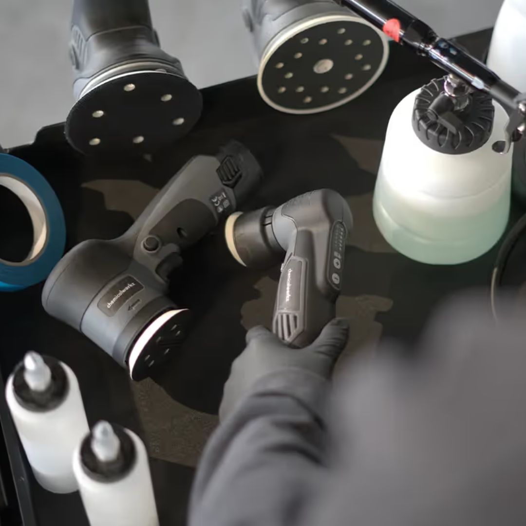 Collection of sanding and polishing tools on a table with a gloved hand.