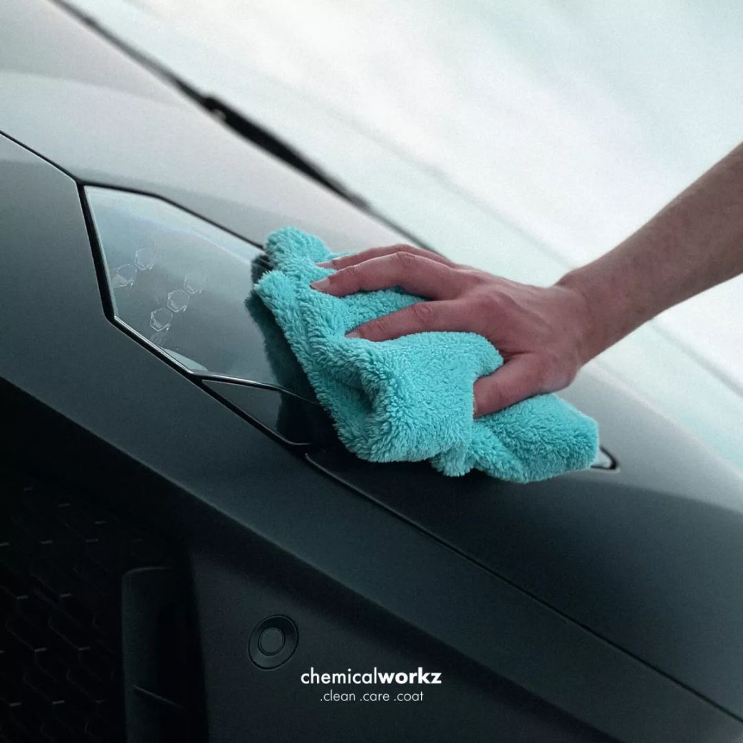 Person cleaning a car window with a teal microfiber cloth, featuring 'chemicalworkz' branding.
