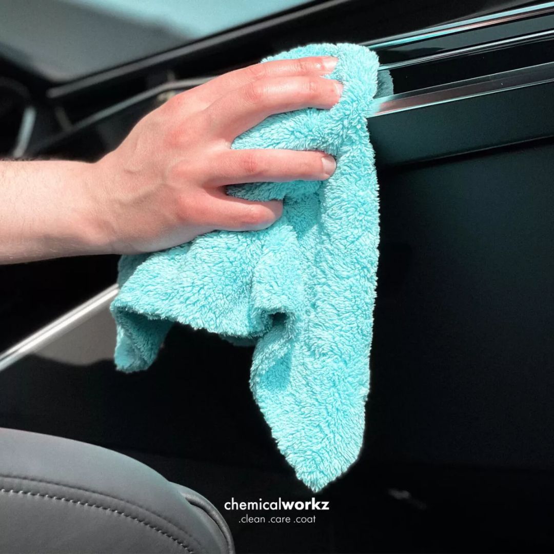Person cleaning a car window with a teal microfiber cloth, featuring 'chemicalworkz' branding.