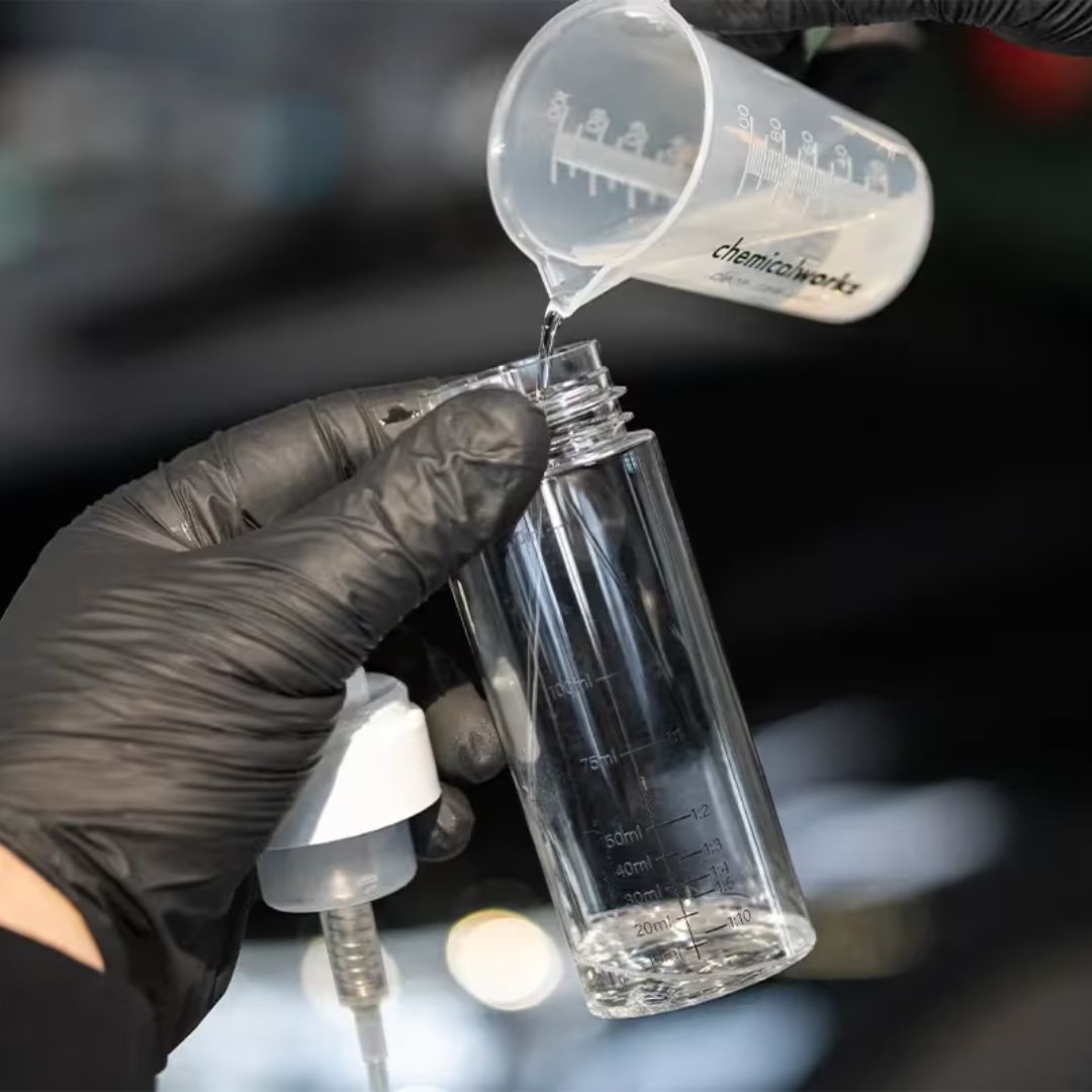 Person pouring liquid from a measuring cup into a clear bottle with a black background