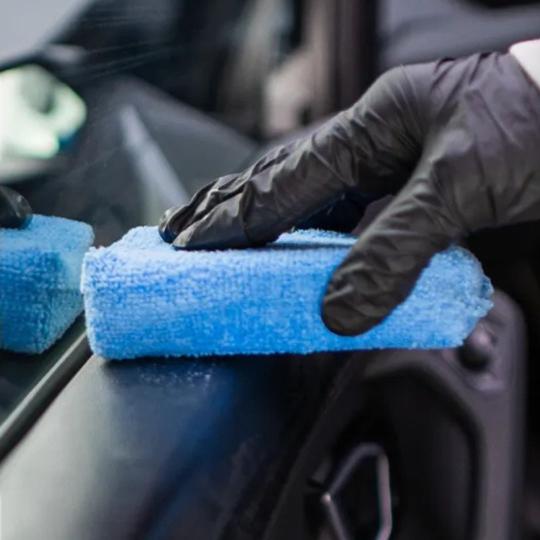 Person cleaning car interior with a blue microfiber towel and black gloves
