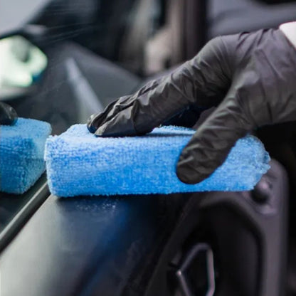 Person cleaning car interior with a blue microfiber towel and black gloves