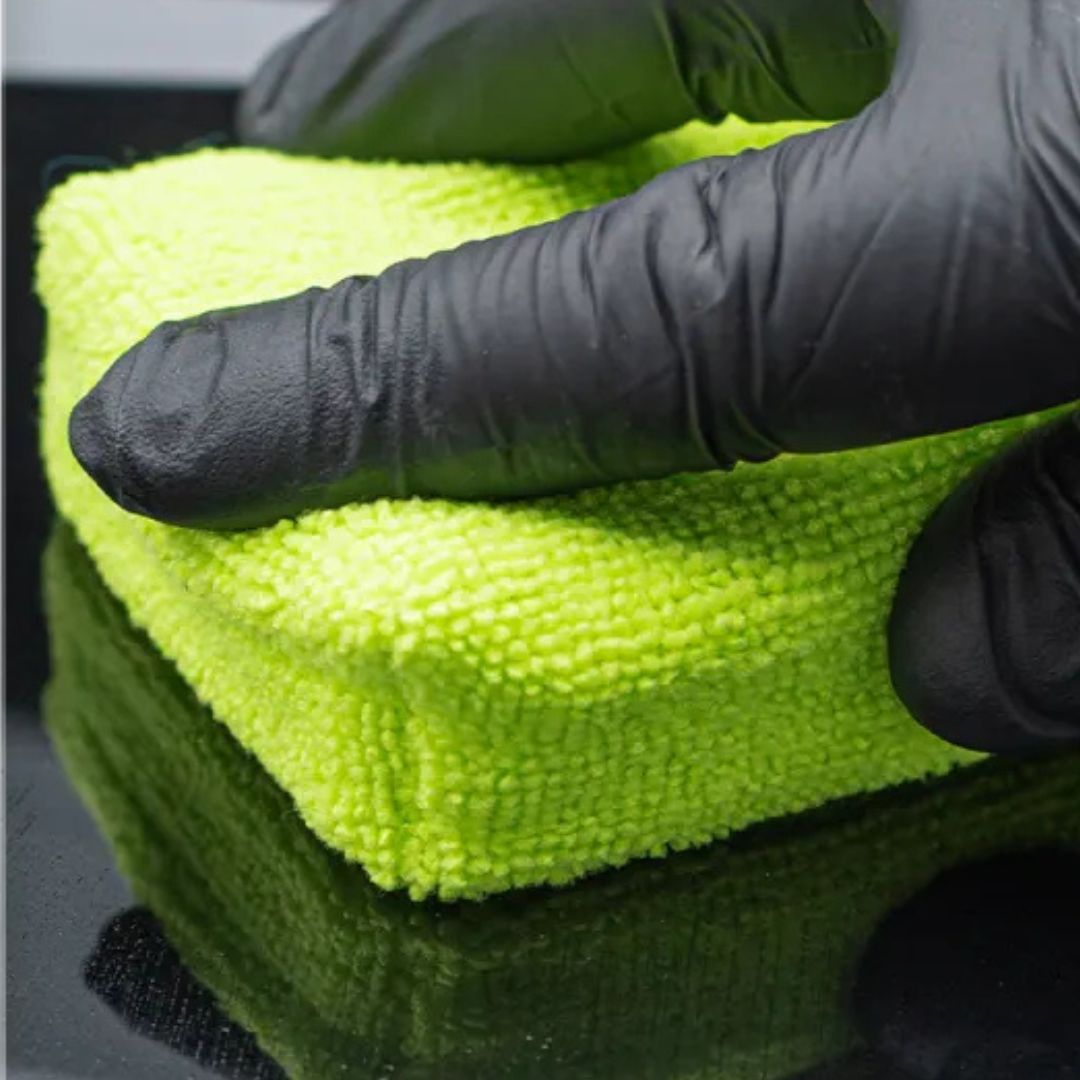 Green microfiber cloth held by a gloved hand on a reflective surface