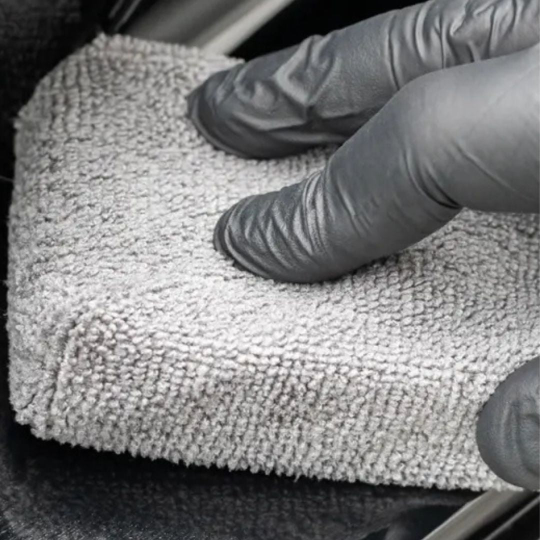 Person wearing gloves cleaning a car interior with a white towel.