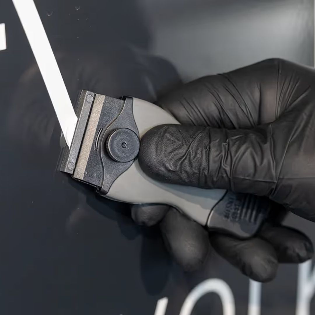 Hand wearing a black glove holding scraper blade tool against a dark background