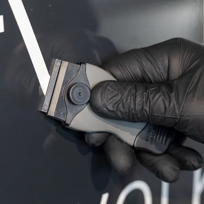 Hand wearing a black glove holding scraper blade tool against a dark background