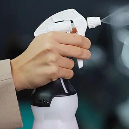 Hand holding a white spray bottle with a black base, spraying a mist against a blurred background.