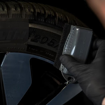 Person wearing a black glove holding a tyre dressing applicator